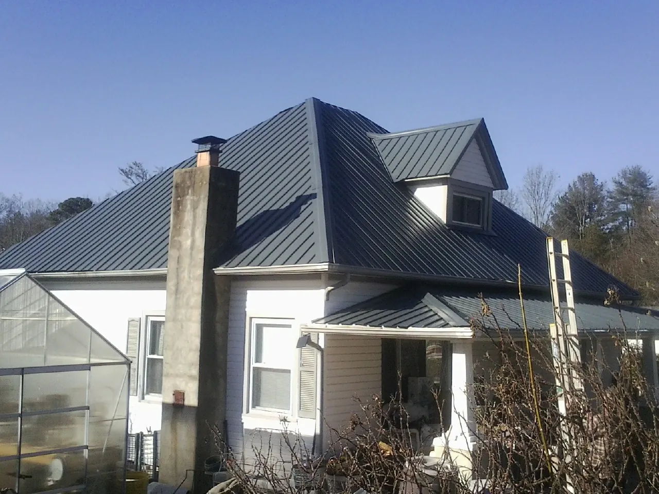 Dark blue standing seam metal roof on a white farmhouse with dormer — Slate & Tile Roof Repair by Roofing Brothers in Camby