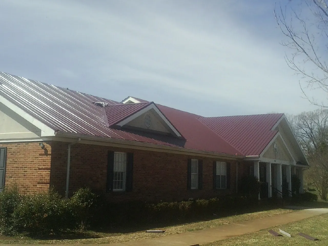 Red metal roof with gabled entries on a long brick building, from a Hail Damage Roof Repair job in Camby