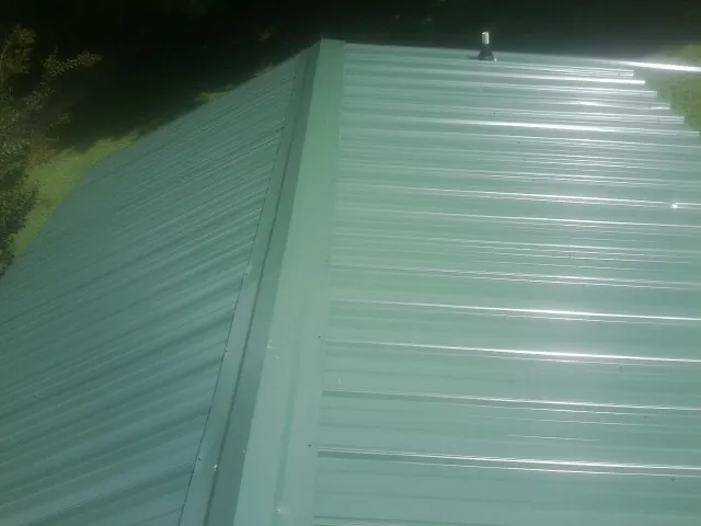New green metal panels meeting at the ridge of a roof — Flat Roof Repair work by our crew in Camby