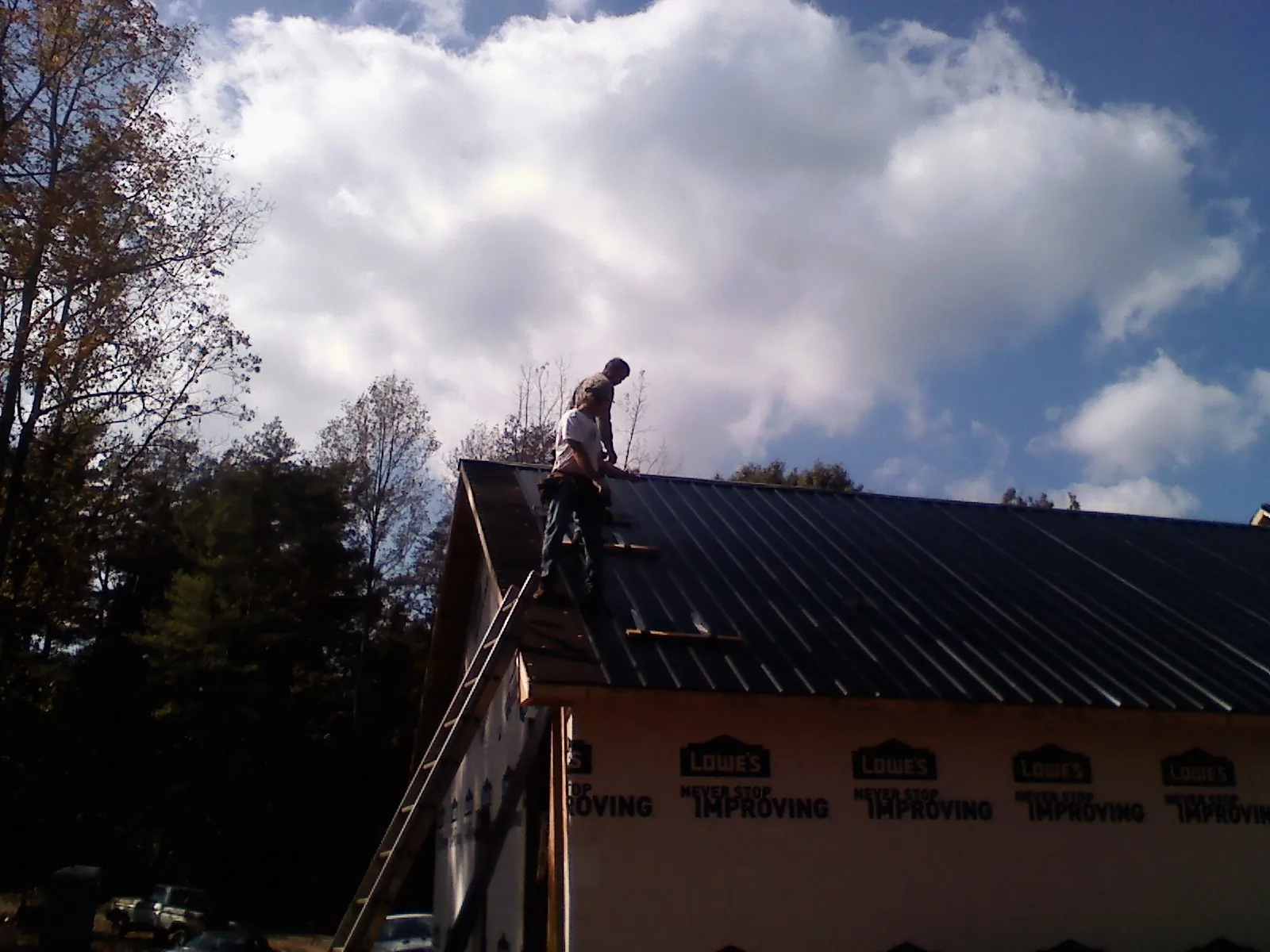 Roofer fastening dark metal panels high against a cloudy sky, from a Roof Inspection job in Camby
