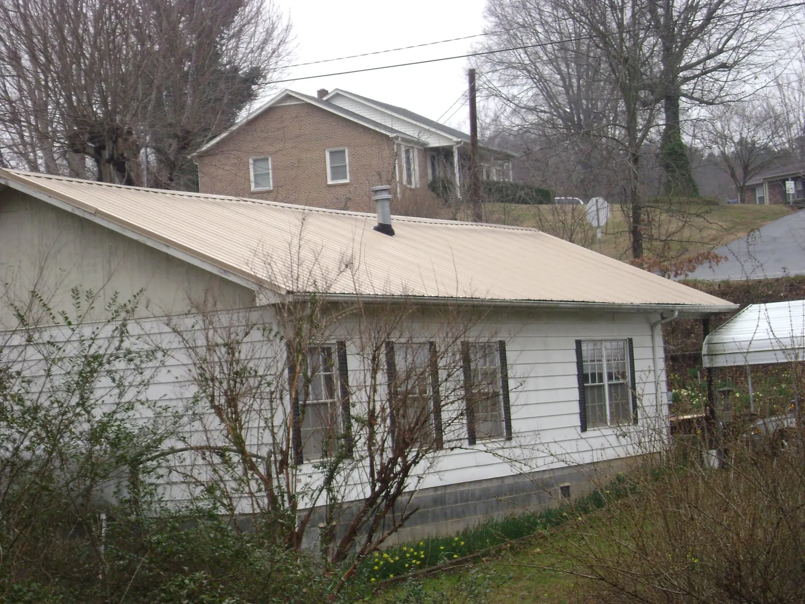 Tan metal roof on a white sided house set into a hillside — Commercial Roofing by Roofing Brothers in Camby
