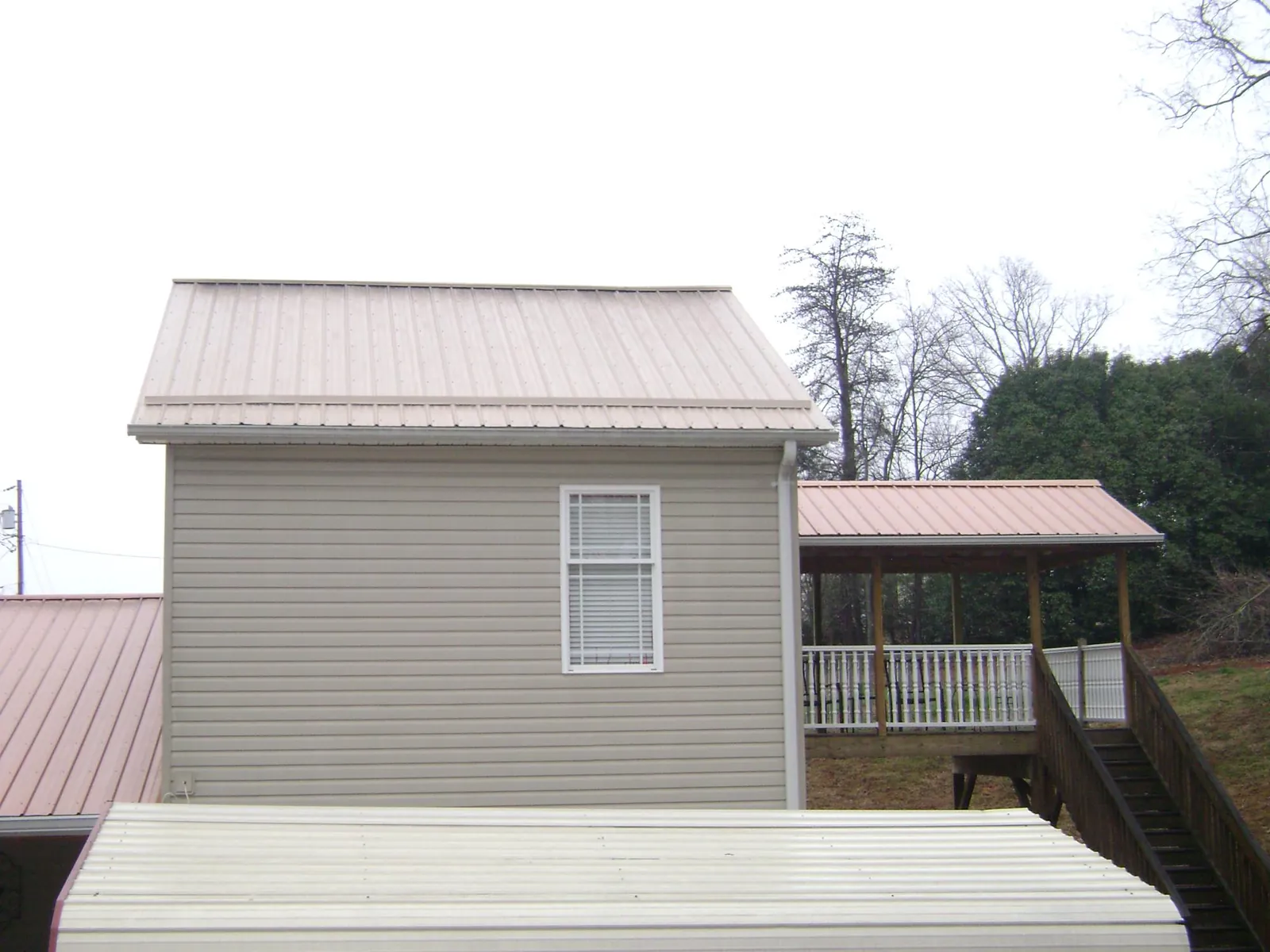 Tan metal roofs on a two story addition and attached porch, from a Roof Replacement job in Camby